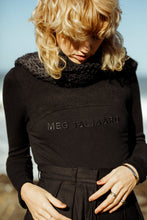 Load image into Gallery viewer, blonde model looking down, wearing a branded meg taljaard, black jersey with high waisted trousers and a black textured scarf accessory