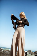 Load image into Gallery viewer, female model wearing beige pants and a black jersey holding a black textured scarf against a blue sky