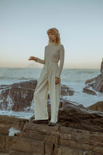 Load image into Gallery viewer, female fashion model standing by the ocean wearing a meg taljaard cream polo neck and high waisted trousers 