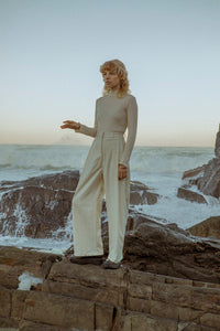 female fashion model standing by the ocean wearing a meg taljaard cream polo neck and high waisted trousers 