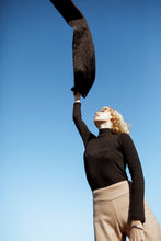 Load image into Gallery viewer, fashion model wearing a black jersey and beige pants throwing a scarf up in the air 