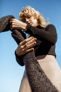 Blonde model against a blue sky holding a black meg taljaard textured scarf accessory 
