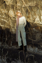 Load image into Gallery viewer, blonde model wearing a meg taljaard polo neck with high waisted trousers and scarf, standing against rocky background 