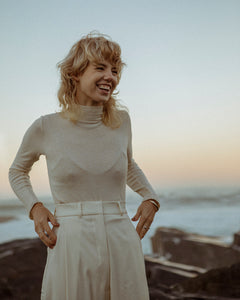 smiling blonde, female model wearing cream polo neck with matching high waisted trousers by meg taljaard