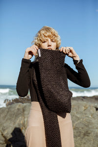 fashion model holding a wide black textured scarf accessory up to her face